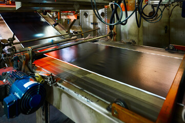 A wide belt of raw rubber compound moves along a roller conveyor. Plant for the production of car tires