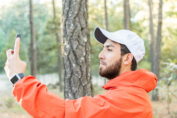 Hombre joven con barba tomando una selfie en el bosque.