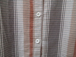 Close-up of a brown shirt's buttoned, emphasizing the fabric's texture and sewing precision. Front...