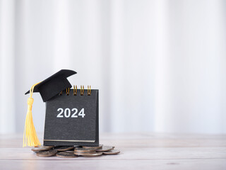 2024 desk calendar with graduation hat on stack of coins. The concept of saving money for education, student loan, scholarship, tuition fees in Year 2024 - obrazy, fototapety, plakaty