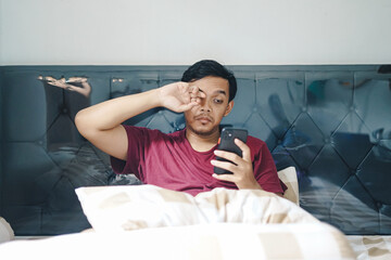 Portrait of Asian Indonesian man rubbing his eye after wake up from sleep