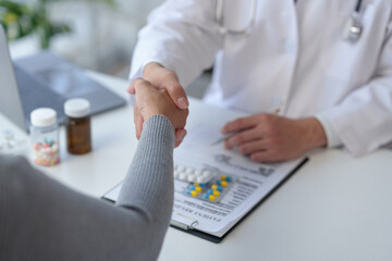Medical service worker or doctor, pharmacist shaking hands with female medical patient at the table...