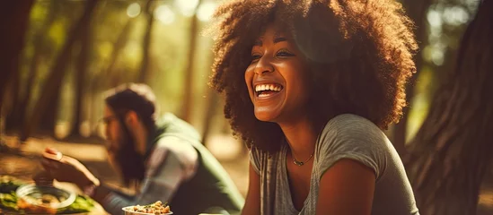 Tuinposter Happy African American woman eating outdoors with friends in a forest. © AkuAku