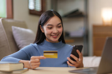 Young asian woman using smartphone and credit card for online shopping at home.