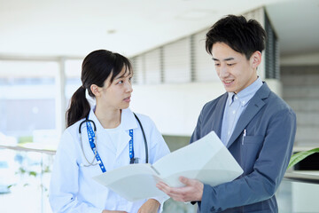 病院内にてスーツを着たMRの男性と話をする女性医師