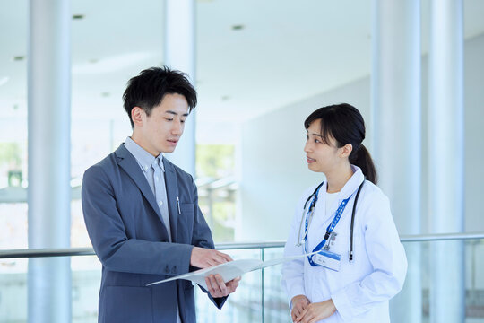 病院内にてスーツを着たMRの男性と話をする女性医師