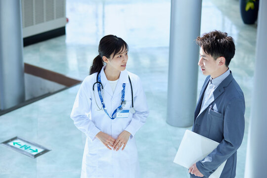 病院内にてスーツを着たMRの男性と話をする女性医師