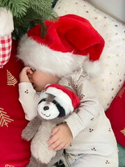 Baby girl with Santa hat sleeping in front of Christmas tree