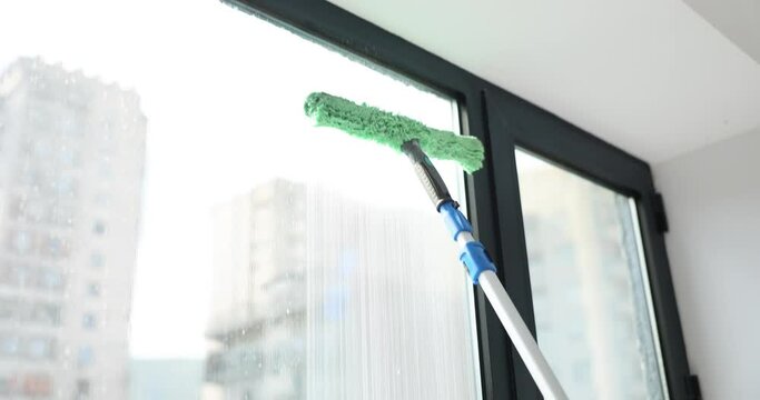 Assistant washes windows with long mop with brush and soapy water