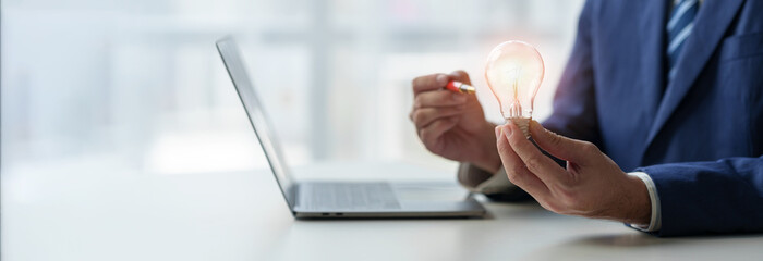 Creative businessman holding a light bulb works on a laptop computer showing new ideas. For...