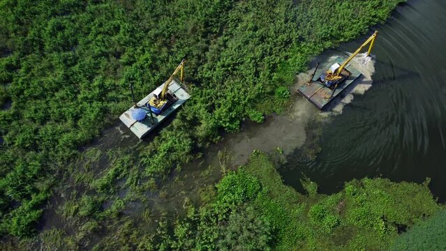 A big excavator in a very large steel ship and a tractor are working in the canal scooping up vegetables and weeds.