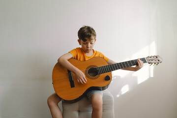 Cute boy learns to play the classical guitar in home. Cozy home. Summer holidays lifestyle.