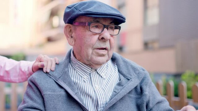 Senior man with beret sitting on wheelchair talking in geriatric