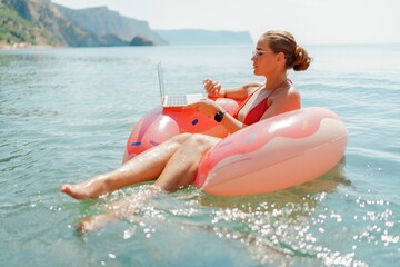 Woman laptop sea. Freelancer woman in sunglases floating on an inflatable big pink donut with a laptop in the sea. People summer vacation rest lifestyle concept