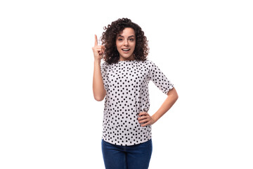 young confident well-groomed brunette curly woman dressed in a blouse with a pattern of peas is...