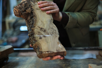 Hands hold a slab of burl wood with intricate grain, highlighting the natural artistry that...