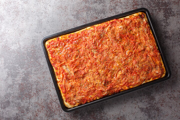 Rectangular Sfincione pizza with onions, tomatoes, cheese, anchovies and breadcrumbs closeup on a baking sheet on the table. Horizontal top view from above