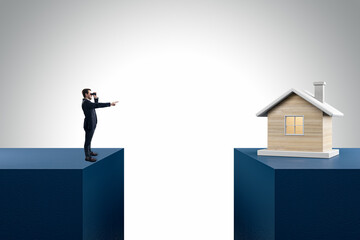 Businessman with telescope pointing at wooden house divided by gap on light background. Mortgage and loan concept.