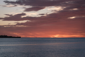 Fototapeta na wymiar Playa de Málaga, amanecer sobre el mar, primeros rayos de sol, al fondo vista del puerto