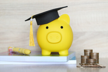 Graduation hat on piggy bank with stack of coins money on wooden background, Saving money for...