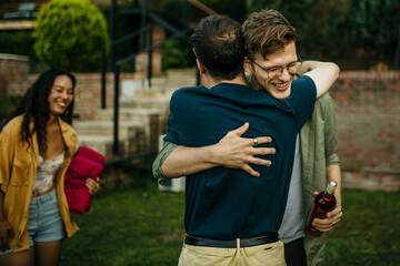 A friendly man with a big smile, waving happily as he greets friends in his cozy backyard