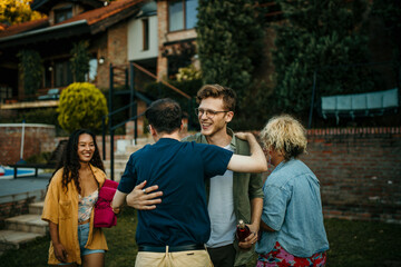 A host joyfully welcomes friends to his home, creating a cheerful atmosphere in the sunny yard