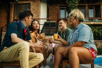 Multiethnic friends gather around the pool, drinks in hand, creating a vibrant atmosphere of laughter and camaraderie