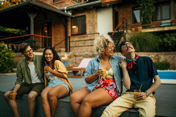 Multiethnic friends gather around the pool, drinks in hand, creating a vibrant atmosphere of laughter and camaraderie