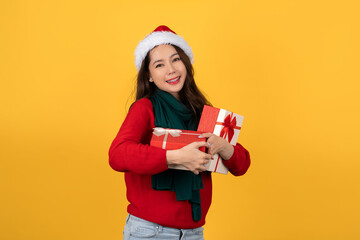 Beautiful young happy Asian woman in Christmas outfit holding red gift box on yellow studio background.