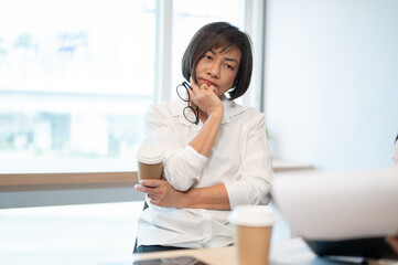 A thoughtful senior Asian female boss is in the meeting, listening to her employee's presentation.