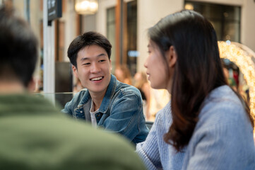 A cheerful young Asian man enjoying talking with his friends while hanging out at a cafe together.
