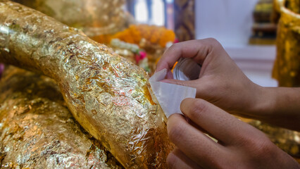 hands pasting gold leaf on back gilded buddha statue.Woman's hands gild behind the Buddha statue.