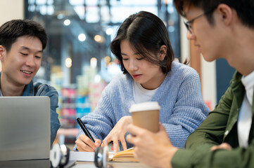 Group of young Asian college students is working on a co-project while sitting in a cafe together.