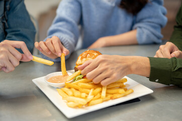 Close-up image of cheerful friends enjoying eating fries at a cafe together, hanging out together.