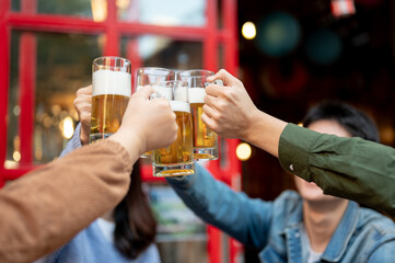 Group of cheerful young Asian friends are cheering and enjoying beer at a restaurant or bar together