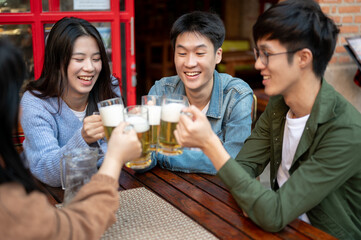 Group of cheerful young Asian friends are cheering and enjoying beer at a restaurant or bar together
