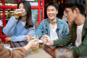 Group of happy Asian friends are enjoying beers at a restaurant or bar in the city together.