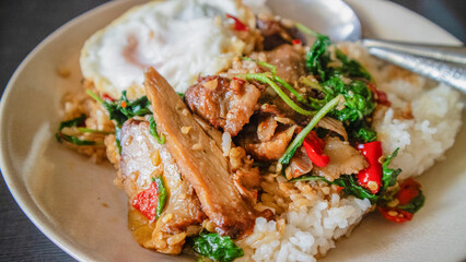 Stir Fried Duck with Holy Basil Beautiful pieces of duck meat, golden brown. Garlic and Basil Placed on a white plate on a cloth on a wooden table with chilli, garlic and basil leaves, Thai