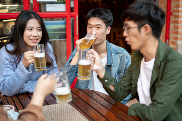 Group of happy Asian friends are enjoying beers at a restaurant or bar in the city together.