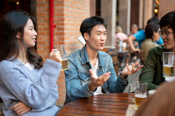 A happy young Asian man is sharing his funny story while enjoying beers with his friends at a bar.