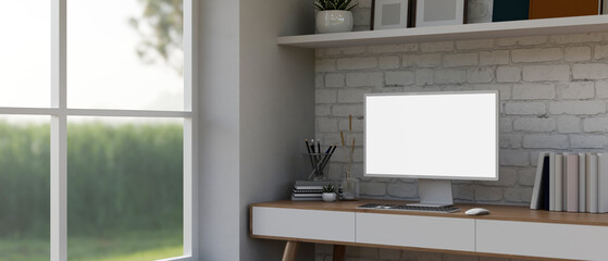 Modern white home office with an empty computer monitor mockup on a desk against a white brick wall.