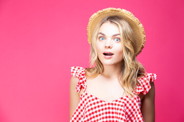 Caucasian Blond Girl In Checked T-shirt and Straw Hat Posing With Surprised Facial Expression Over Coral Pink Background.