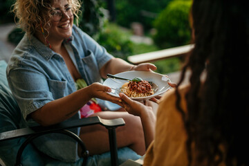 Two female friends passing a pasta plate to each other