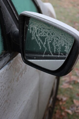 Car mirror on side view of gray car covered by heavy frost on winter season