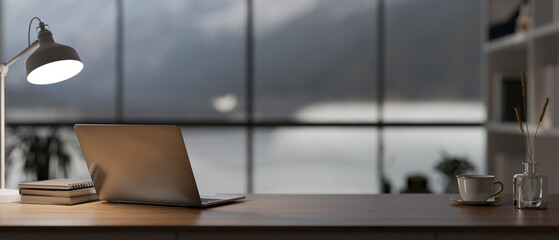 A laptop computer, a table lamp, and decor on a wooden desk in a modern, luxury CEO office room.