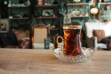 A golden decorated glass of Turkish tea on an elegant glass plate with a spoon inside - artistic gallery cafe background