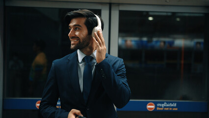 Closeup of smart executive manager listen relaxing music while waiting at train station. Happy male...