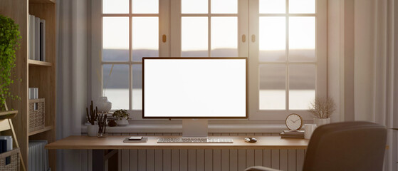 Modern home workstation, a PC computer white screen mockup on a wooden desk against the window.