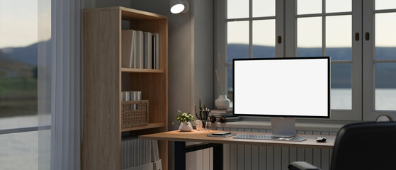 Modern home office workspace with a computer mockup on a desk and a bookshelf near by the window.