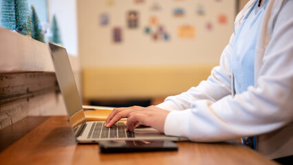 Side view image of a woman using her laptop computer at a table in a coffee shop.